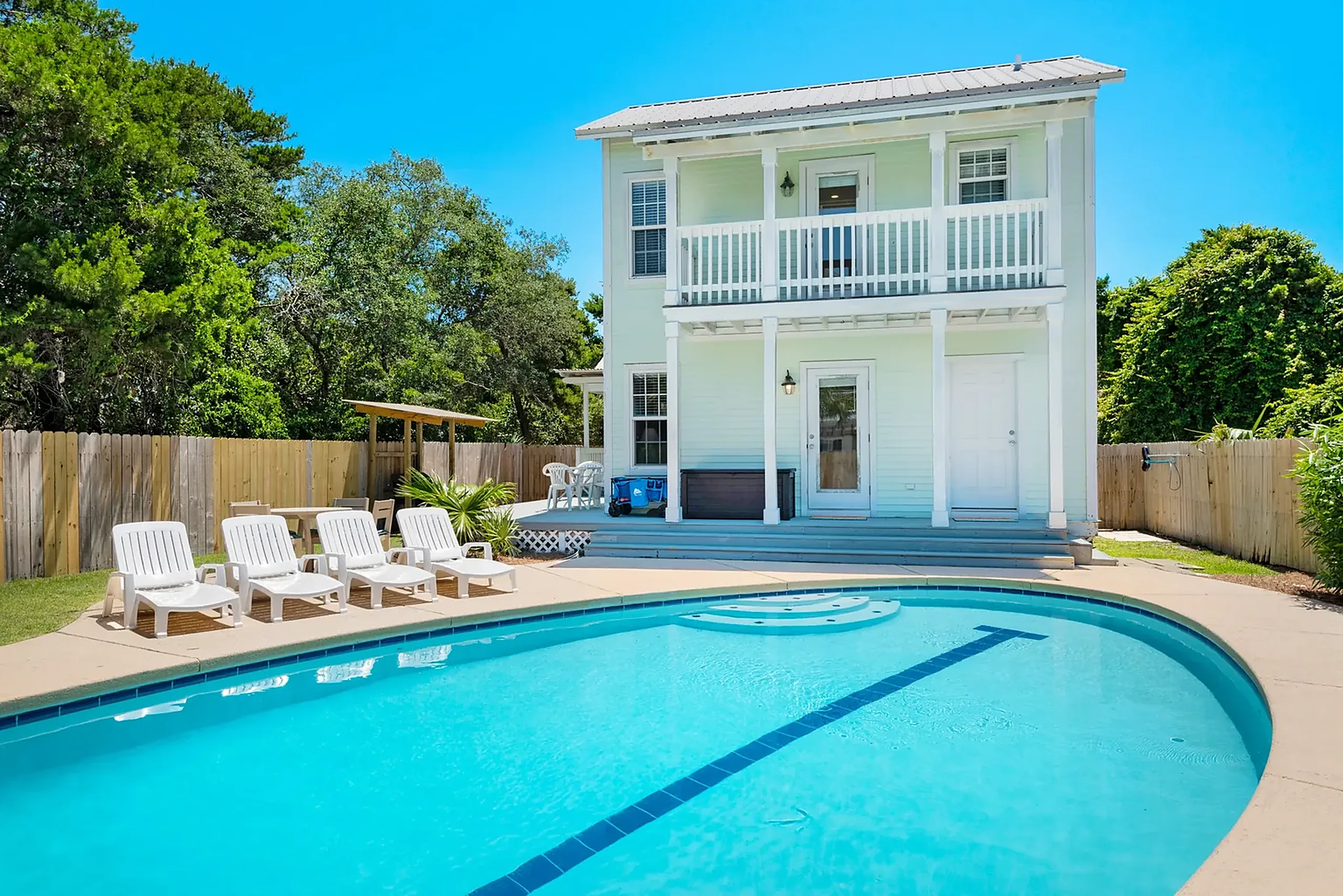 Two story white coastal vacation home with a double porch above a kidney shaped pool and white loungers